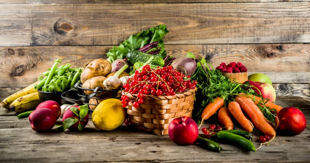 Friss zöldségek és gyümölcsök egy asztalon: répa, alma, bogyós gyümölcsök és leveles zöldségek, tudatos étkezés és életmódváltás szemléltetésére.
