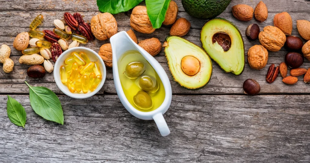 Egészséges zsiradékforrások egy asztalon: olívaolaj, avokádó és olajos magvak, tudatos táplálkozás és életmódváltás szemléltetésére.